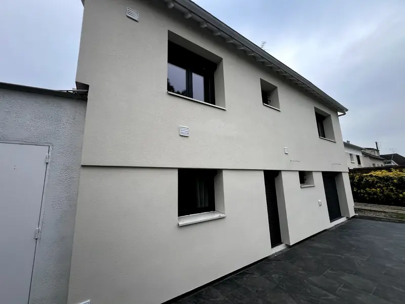 Maison à étage après isolation par l'extérieur, enduit gris clair et encadrements de fenêtres