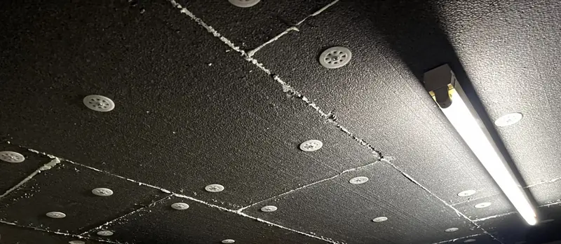 Panneaux isolants chevillés au plafond d'un sous-sol, sous un plancher d'habitation